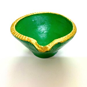 A studio shot on a plain white background of a single hand-painted green terracotta diya. The product features an organic, single-wick pour spout design with a smooth interior base and a thick, metallic gold-painted rim highlighted by engraved braided texture details.