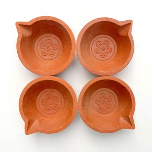Puede incluir: Cuatro lámparas diya de terracota con un diseño floral. Las diyas son lámparas tradicionales indias que se utilizan durante festivales como Diwali.
