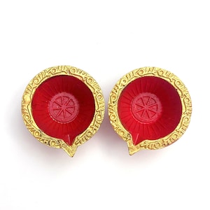 May include: Two red and gold diya lamps, traditional Indian oil lamps used during Diwali celebrations.