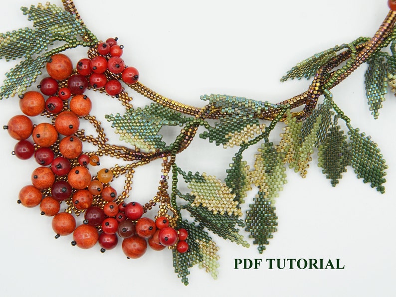 May include: A beaded necklace with a cluster of red and orange beads, resembling berries, and green leaves. The necklace is made with seed beads and features a delicate, intricate design. The text "PDF TUTORIAL" is visible at the bottom of the image.