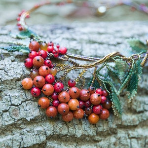 May include: A beaded necklace with a leafy design and red berries. The necklace is made with small beads and is a beautiful example of handmade jewelry.