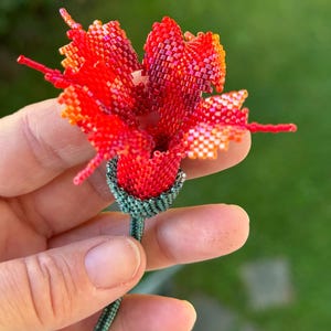 Könnte beinhalten: Eine Perlenblume mit roten, orangefarbenen und gelben Blütenblättern und einem grünen Stiel. Die Blume ist aus kleinen Perlen gefertigt und sehr detailliert.