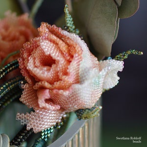 Könnte beinhalten: Nahaufnahme einer zarten, perlenbesetzten Rose aus schimmernden rosa und weißen Perlen. Die Rose steht in einer Vase mit grünen Perlenblättern.