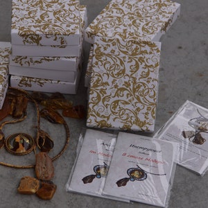 May include: A collection of amber necklaces and earrings displayed on a table with white boxes and instructions in Russian. The jewelry is packaged in white boxes with a gold floral pattern. The instructions are printed on white paper with a clear plastic cover.