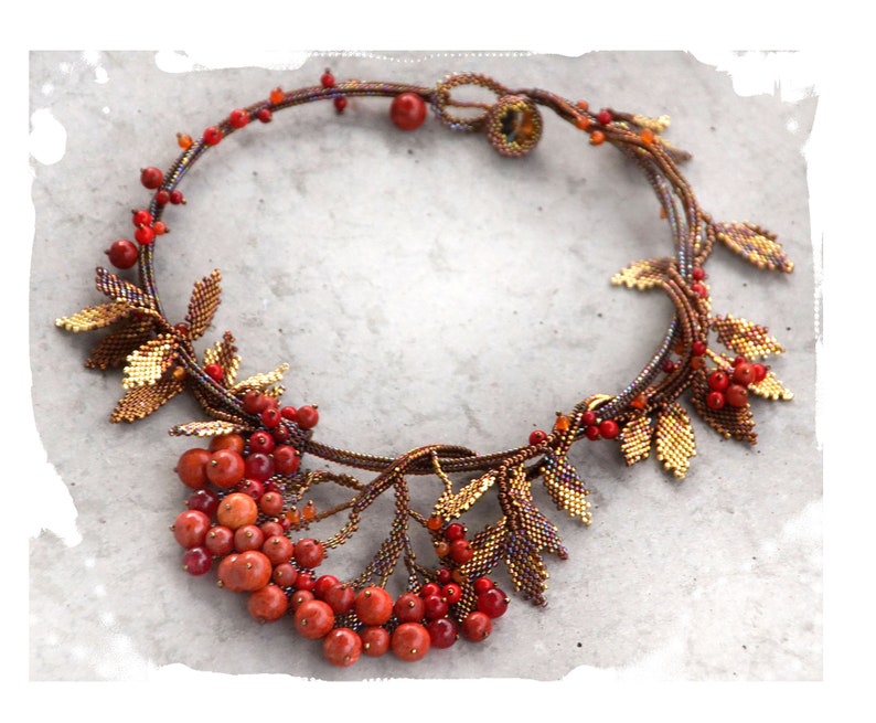 May include: A beaded necklace with a design of leaves and berries. The leaves are gold and brown, and the berries are red.