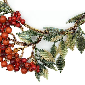 May include: A beaded necklace with a cluster of red and orange berries and green leaves. The necklace is made of small beads and is a beautiful example of beadwork.