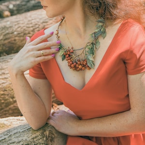 May include: A woman wearing a red dress with a unique necklace made of leaves and red berries.
