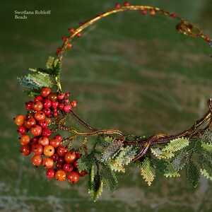 May include: A beaded necklace with a design of a branch with red berries and green leaves. The necklace is made of small beads and is a beautiful piece of jewelry.