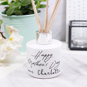 May include: White ceramic diffuser bottle with a silver lid and wooden sticks. The bottle has black text that reads "Happy Mother's Day Love Charlotte".