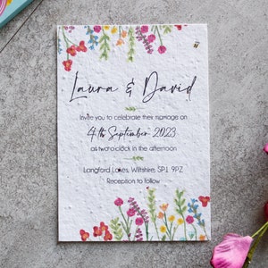 May include: Wedding invitation card with a floral border and the text "Laura & David" printed in black. The invitation details the wedding date as "4th September 2023" and the location as "Langford Lakes, Wiltshire, SP1 9PZ".