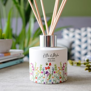 May include: White ceramic diffuser bottle with a silver lid and wooden sticks. The bottle has a floral design with a bee and butterfly. The text "Katie & Mike New Home 30.05.2021" is printed on the bottle.