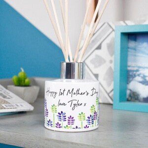 May include: White ceramic diffuser bottle with a silver lid and wooden sticks. The bottle has a floral design and the text "Happy 1st Mother's Day love Tyler x".