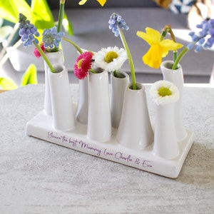 May include: White ceramic flower vase with six openings for flowers. The vase has a base with the inscription "You're the best Mummy. Love Charlie & Eva".