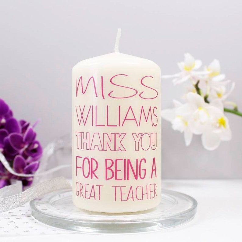Op de afbeelding: Witte kaars in de vorm van een pilaar met roze tekst die "Miss Williams Thank You For Being A Great Teacher" zegt.