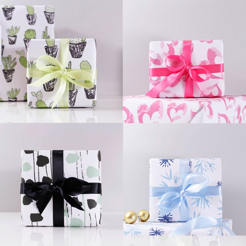May include: Four gift boxes wrapped in different patterned paper. The boxes are arranged in a grid pattern on a white surface. The top left box is wrapped in white paper with a black and green cactus pattern. The top right box is wrapped in white paper with a pink heart pattern. The bottom left box is wrapped in white paper with a black and green abstract pattern. The bottom right box is wrapped in white paper with a blue snowflake pattern.