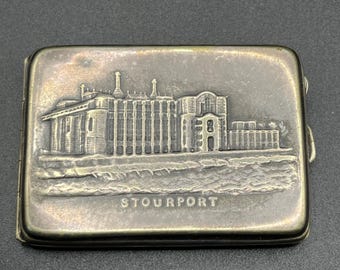 Op de afbeelding: Een rechthoekige, zilverkleurige metalen doos met een gedetailleerde reliëf afbeelding van een gebouw en het woord "STOURPORT" onderaan. De doos heeft een scharnierend deksel en een sluiting aan de zijkant.
