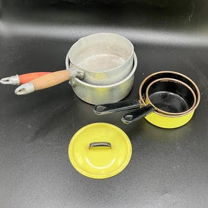 Peut inclure: Ensemble de casseroles vintage en aluminium et un couvercle jaune. Les casseroles ont des poignées en bois avec des accents rouges. Un ensemble de casseroles est jaune avec des poignées noires. Le couvercle est jaune avec une poignée noire.