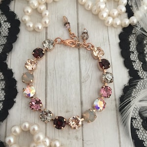 May include: A rose gold bracelet with a chain and a row of colorful crystal beads. The beads are in shades of pink, red, and white.
