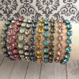 May include: A set of ten colorful crystal bracelets with a silver chain. The bracelets are arranged in a row, with the colors ranging from pink to blue.