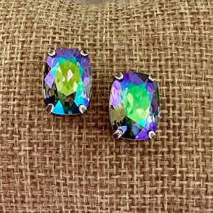 May include: A pair of iridescent green and blue square-shaped earrings on a burlap cushion.