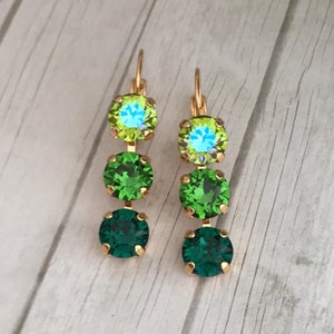 May include: A pair of gold dangle earrings with four green and light green crystal stones. The stones are round and faceted.