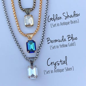 May include: Three necklaces with rectangular crystal pendants. The top necklace has a clear crystal pendant set in antique brass, the middle one has a blue crystal set in yellow gold, and the bottom one has a clear crystal set in antique silver.