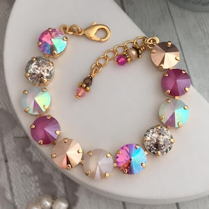 May include: A gold bracelet with a chain and a clasp. The bracelet is adorned with round, iridescent crystals in shades of pink, white, and gold.