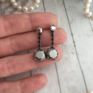 May include: A pair of silver dangle earrings with black crystal accents. The earrings feature a large round black crystal at the bottom and a smaller black crystal at the top.