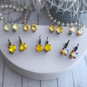 May include: Assortment of yellow and iridescent crystal earrings with silver and gold tone findings. The earrings are displayed on a white surface.