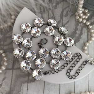 May include: A silver chain necklace with a crystal pendant. The pendant is made up of multiple round crystals arranged in a circular pattern.