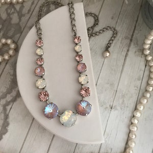 May include: A silver chain necklace with a graduated row of iridescent pink and white crystal beads. The necklace is displayed on a white stand.