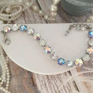 May include: A silver bracelet with iridescent crystals in shades of white and blue. The bracelet has a lobster claw clasp.