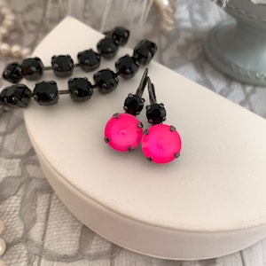 May include: A pair of hot pink drop earrings with black accents. The earrings feature a round, vibrant pink stone at the bottom and a smaller black stone at the top. A matching black stone bracelet is also visible.