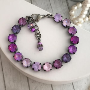 May include: A purple and lavender crystal bracelet with a silver clasp. The bracelet is made of small, round crystals that are set in silver.