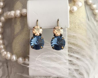 May include: A pair of dangle earrings with two crystal stones. The top stone is a light peach color and the bottom stone is a dark blue color. The earrings are on a white display card.