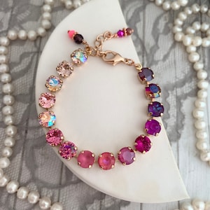 May include: A delicate gold bracelet with a gradient of pink and purple crystals. The bracelet is made with small, round crystals that are set in a row. The crystals are iridescent and sparkle in the light.