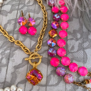 Pode incluir: Um colar de corrente de ouro com um grande pingente quadrado de pedra preciosa laranja iridescente e um fecho de trava. O colar &eacute; combinado com um bracelete de cristal rosa e iridescente e brincos combinando.