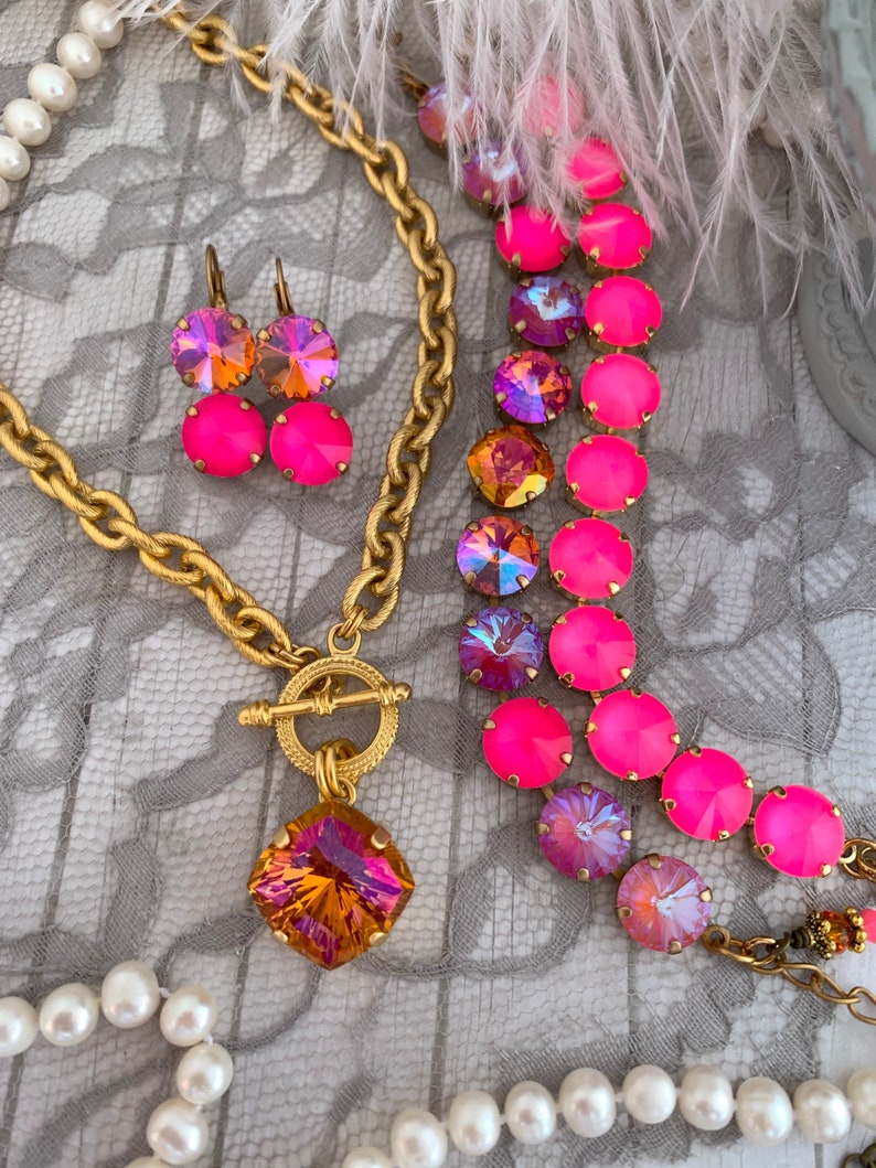 Pode incluir: Um colar de corrente de ouro com um grande pingente quadrado de pedra preciosa laranja iridescente e um fecho de trava. O colar &eacute; combinado com um bracelete de cristal rosa e iridescente e brincos combinando.