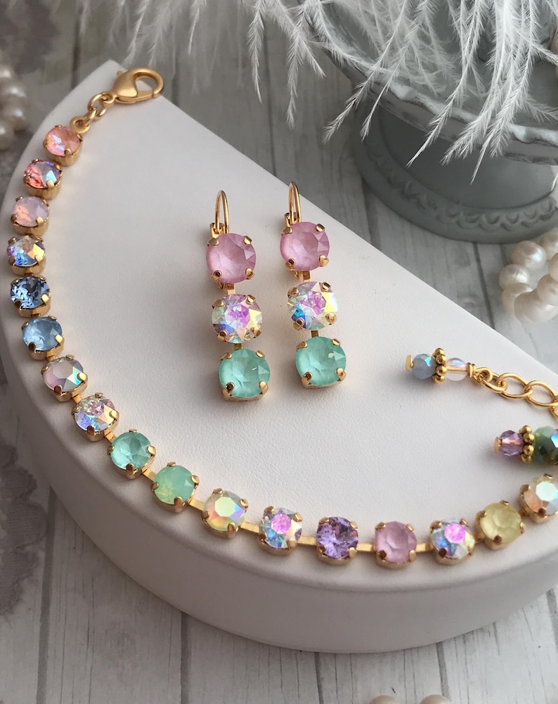 May include: A set of pastel-colored crystal earrings and a bracelet. The earrings are made of three crystals each, in shades of pink, light blue, and green. The bracelet is made of a chain of crystals in a rainbow of colors, including pink, light blue, green, yellow, and purple.