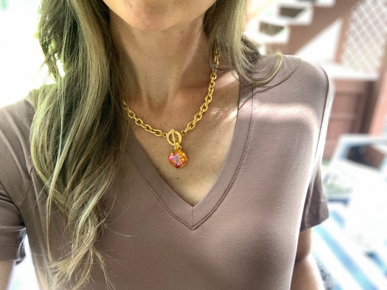 Pode incluir: Um colar de corrente de ouro com um pingente quadrado de pedra preciosa rosa e laranja.