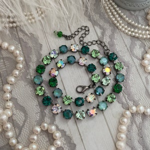 Peut inclure: Un collier délicat avec un design dégradé ombré de cristaux verts et irisés. Le collier est réalisé avec une chaîne en métal noir et une fermeture à fermoir.