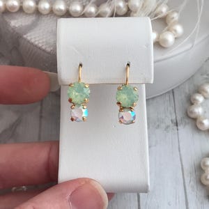 Könnte beinhalten: Ein Paar goldene Ohrringe mit zwei runden, grünen und schillernden Steinen.