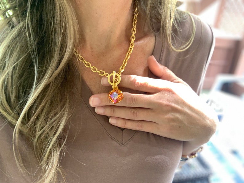 Pode incluir: Um colar de corrente de ouro com fecho de trava e um pingente quadrado com uma gema multicolorida.