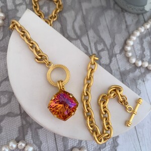 Pode incluir: Um colar de corrente de ouro com um grande pingente de pedra preciosa facetada laranja e rosa. A corrente tem um design texturizado tipo corda e um simples anel redondo de ouro na parte superior do pingente.