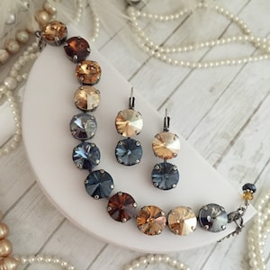May include: A set of jewelry featuring a necklace and earrings with a gradient of blue and amber crystal stones. The necklace and earrings are made with silver-toned metal.