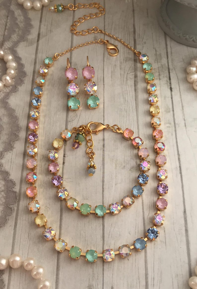May include: A set of pastel rainbow colored crystal jewelry, including a necklace, bracelet, and earrings. The jewelry is made with gold-toned metal and features iridescent crystals.