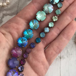 May include: A collection of iridescent crystal jewelry in shades of blue, purple, and pink. The crystals are set in copper-colored metal and arranged in a cascading design. A pearl necklace is visible in the background.