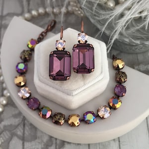 May include: A pair of rectangular purple crystal drop earrings with copper-toned settings and a matching bracelet featuring a series of round, multi-colored, and purple crystals set in copper-toned metal links.