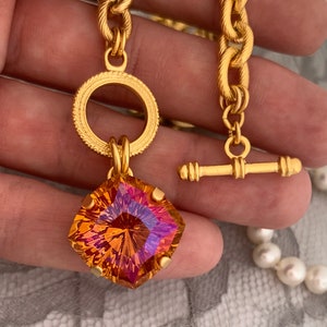 Pode incluir: Um colar de corrente de ouro com um grande pingente de pedra preciosa facetada laranja e roxa. O pingente &eacute; preso a um anel de ouro com uma borda decorativa. O colar tem um fecho de trava de ouro.