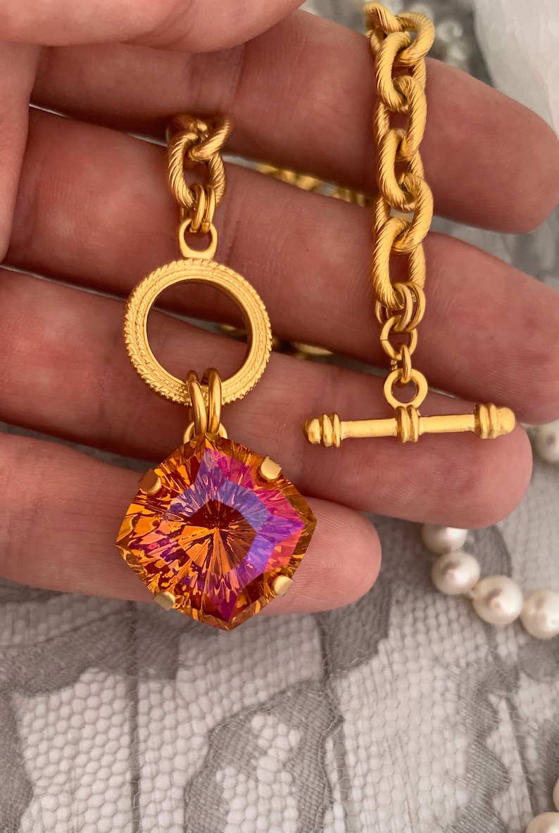 Pode incluir: Um colar de corrente de ouro com um grande pingente de pedra preciosa facetada laranja e roxa. O pingente &eacute; preso a um anel de ouro com uma borda decorativa. O colar tem um fecho de trava de ouro.